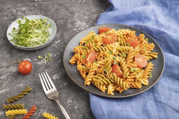 Tortiglioni semolina pasta with tomato and microgreen sprouts on a black concrete background and