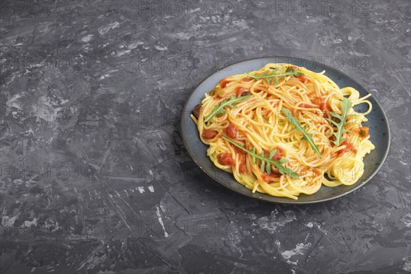 Corn noodles with tomato sauce and arugula on a black concrete background. Side view, close up,