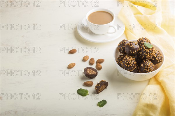 Chocolate caramel ball candies with almonds and a cup of coffee on a white wooden background and
