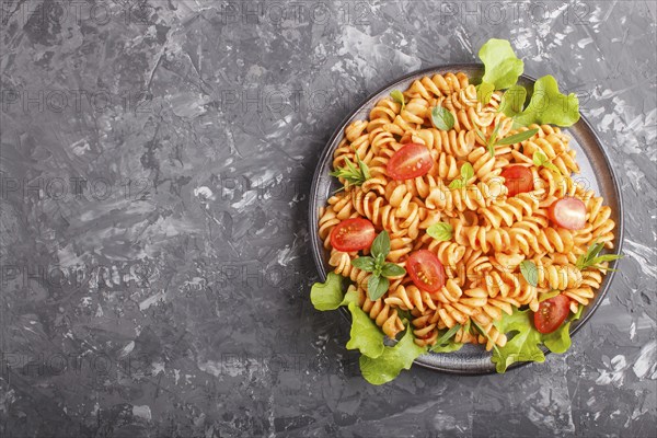 Fusilli pasta with tomato sauce, cherry tomatoes, lettuce and herbs on a black concrete background.