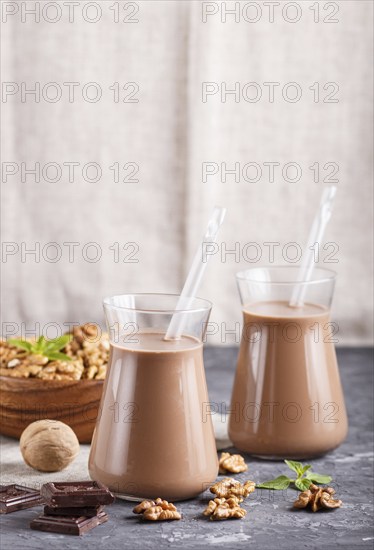 Organic non dairy walnut chocolate milk in glass and wooden plate with walnuts on a black concrete