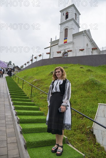 Young woman in folk traditional costume in front of a church on a green hill, woman in traditional