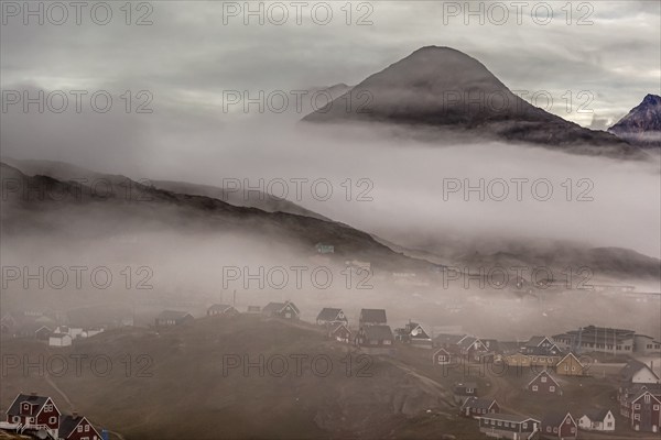 Inuit settlement, houses in the fog in front of steep mountains, Tasiilaq, East Greenland,