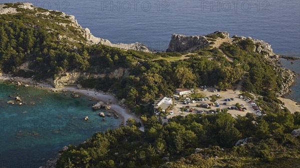 Car park and building in a rocky coastal landscape surrounded by trees and clear blue water,