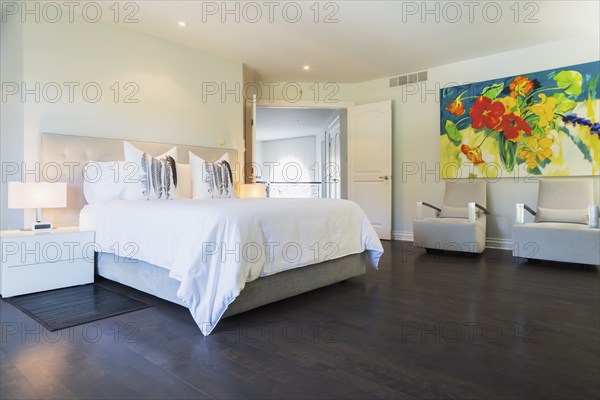 Master bedroom with queen size bed, white lacquered nightstands, upholstered armchairs and dark