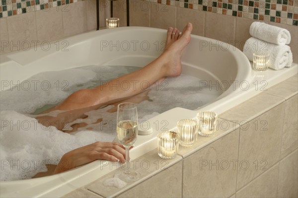 Woman relaxing in the bathroom spa tub with a glass of sparkling champagne and candles