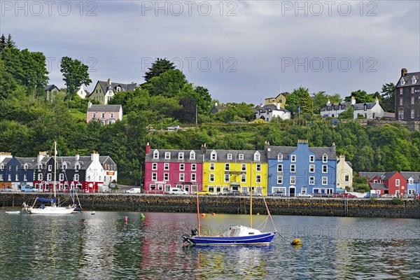 Houses with colourful facades along a harbour, boats in the foreground and a green hill in the