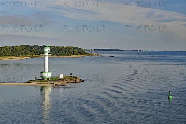White-green lighthouse on a coast with wide water surfaces and a green buoy in the foreground,