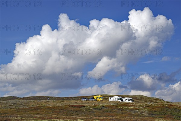 Motorhomes on a hilly landscape under large, dramatic cloud formations in the blue sky, autumn,