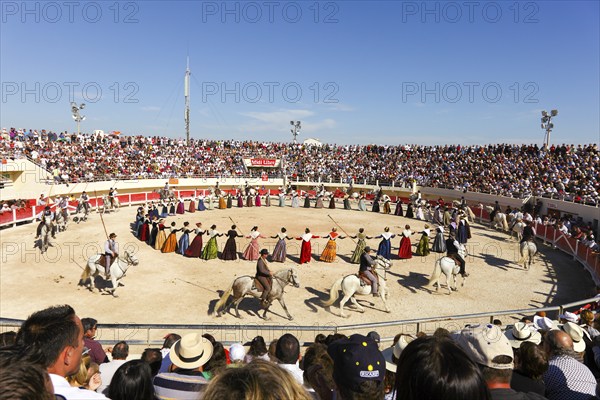 Women dance in traditional costumes and men ride horses in the arena of Les Saintes Maries de la