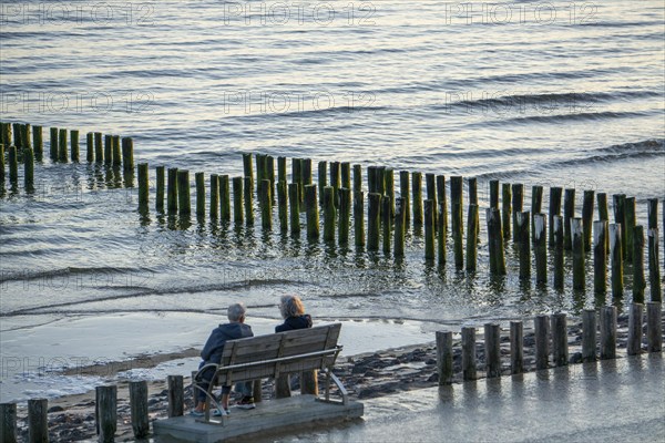 Two elderly woman on a bench on the beach, at high tide, breakwater, Netherlands