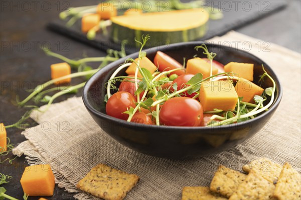 Vegetarian vegetable salad of tomatoes, pumpkin, microgreen pea sprouts on black concrete