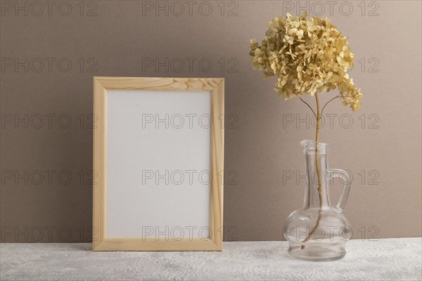 White wooden frame mockup with dried hydrangea in glass on beige paper background. Blank, vertical