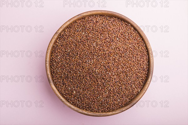 Wooden bowl with raw red quinoa seeds on a pastel pink background. Top view, flat lay, close up