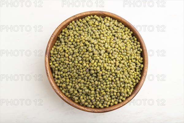 Wooden bowl with raw green mung bean on a white wooden background. Top view, flat lay, close up