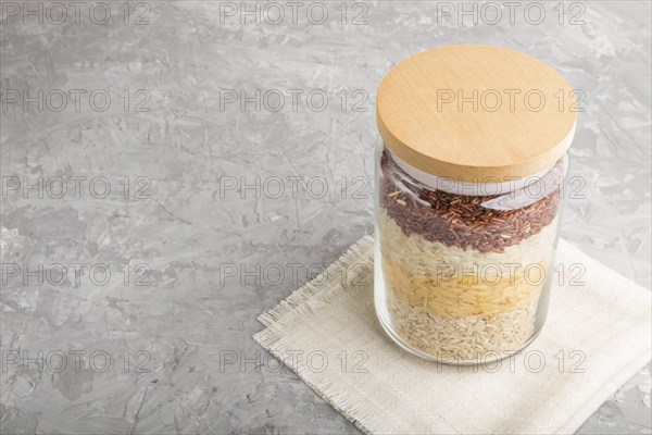 Glass jar with different kinds of rice poured in layers on a gray concrete background. side view,