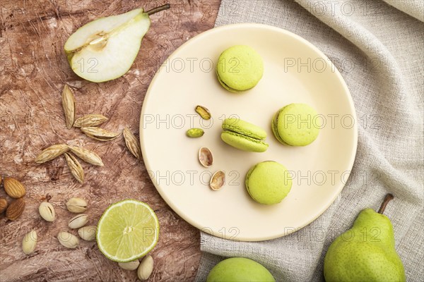 Green macarons or macaroons cakes with cup of coffee on a brown concrete background and linen