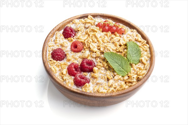 Wheat flakes porridge with milk, raspberry and currant in wooden bowl isolated on white background.