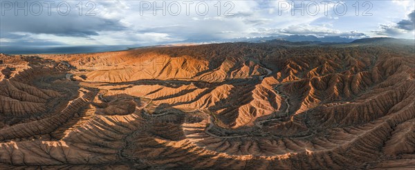 Panorama, landscape of eroded hills at Lake Issyk Kul, badlands at sunset, mountain peaks of the