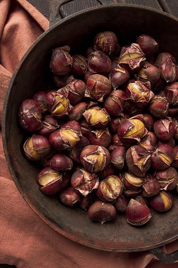 Roasted chestnuts, in an iron pan, wooden table, top view, no people, rustic style