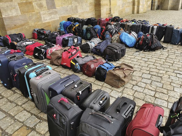 The luggage of a group of travellers stands in rows on the pavement, outside, suitcases and bags