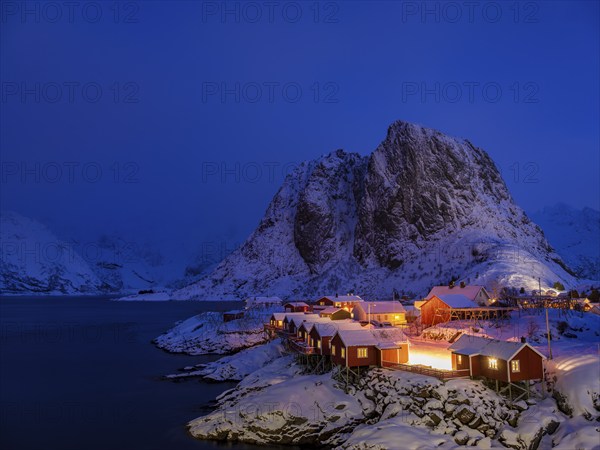 Rorbuer huts of Hamnoy at the fjord at dusk, snowy mountains in the background, Hamnøy, Reine,