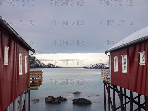 View between two traditional red wooden houses across the fjord to the mountains of the mainland,