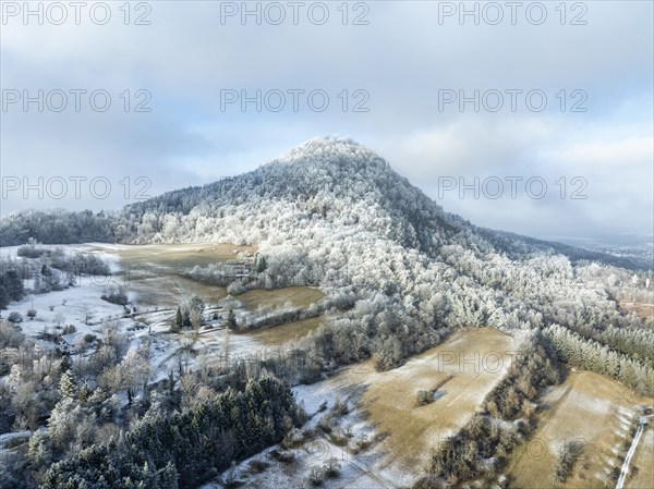Aerial view of the snow-covered Hegau volcano Hohenhewen, surrounded by frosty trees in a winter