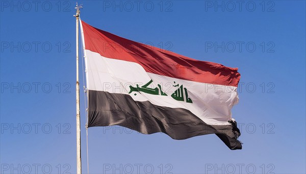 The flag of Iraq flutters in the wind, isolated against a blue sky