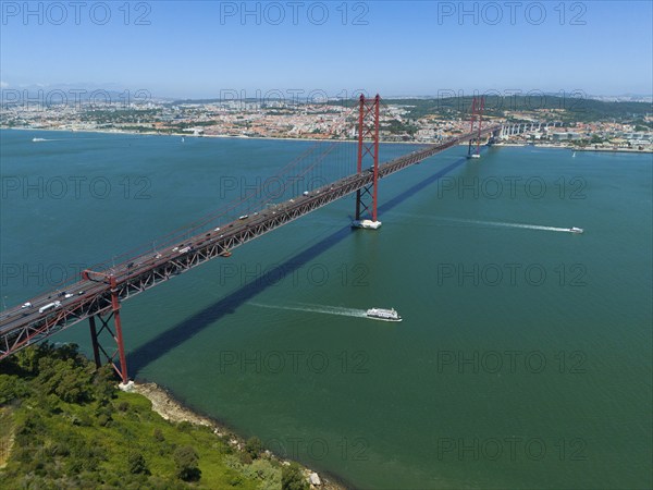 Red bridge spanning the water, lined with boats, with a city and nature in the background on a
