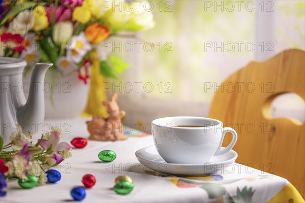 A coffee cup on a table with Easter decorations and a colourful bouquet of spring flowers in the
