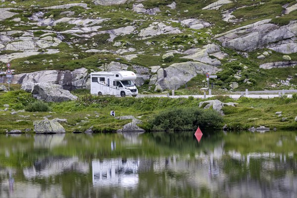 Gotthard Pass, top of the pass. A motorhome is reflected in a mountain lake. Airolo, Canton Ticino,