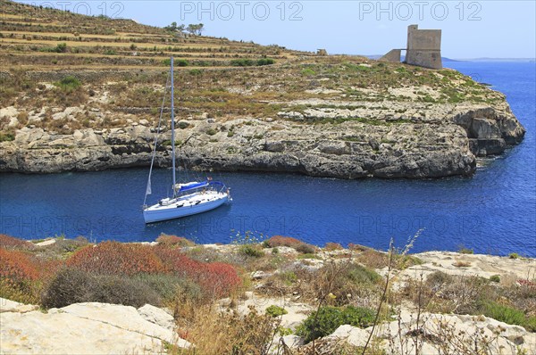 Yacht and watchtower at entrance to Mgarr ix-Xini coastal inlet, island of Gozo, Malta, Europe