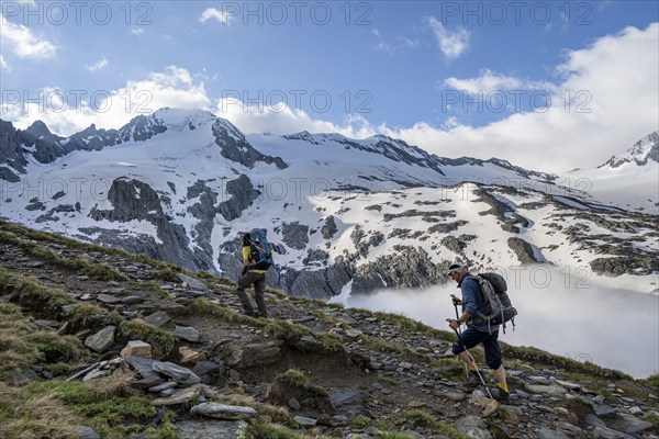 Two mountaineers on a hiking trail, high fog in the valley, glaciated mountains with