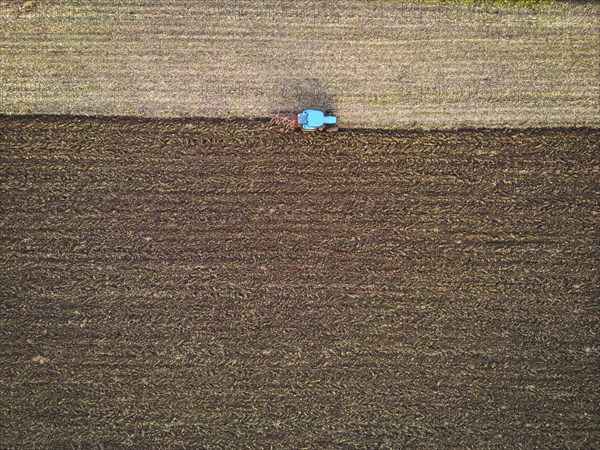 Aerial view of a tractor ploughing a field, a farmer in a modern tractor ploughing field on a sunny