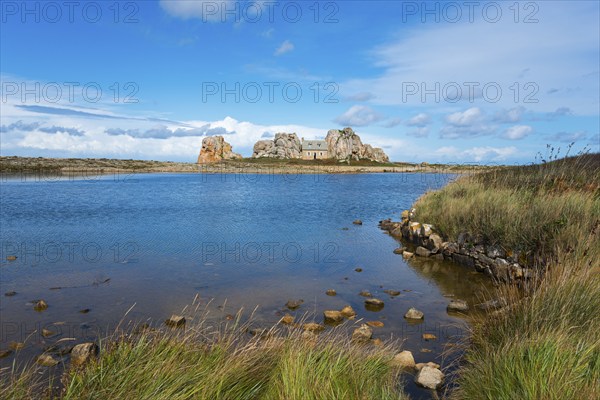 A house stands between rocks on a lake under a blue sky with clouds, House between the rocks on the