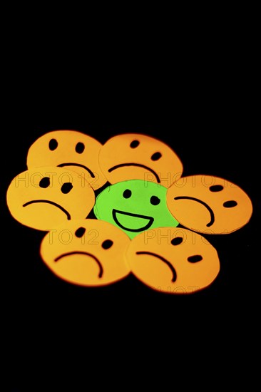 Paper cutouts of sad smileys surrounding a happy smiley. concept of positivism, social problems,
