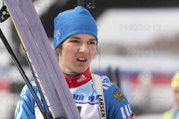 Sportswoman biathlete Soenko Violetta with skis in hands and rifle behind her after skiing and