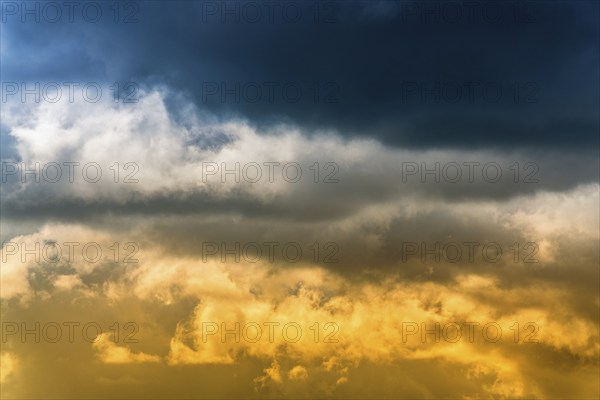 Dramatic blue thunderclouds on top and yellow-golden fluffy clouds illuminated by rays of sun on