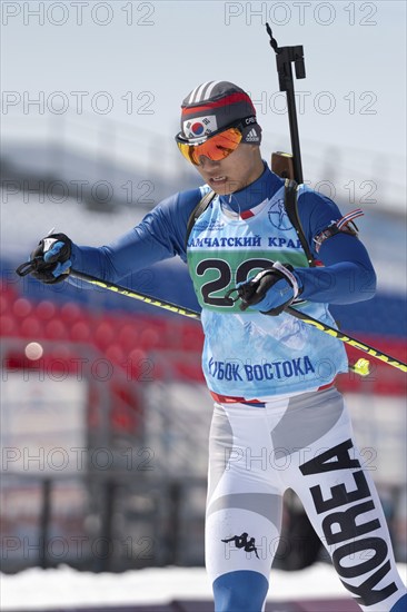 Sportsman biathlete Cheon Yunpil South Korea skiing on ski track distance biathlon arena. Junior