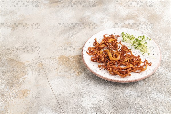 Fried Cordyceps militaris mushrooms on brown concrete background with microgreen, herbs and spices.