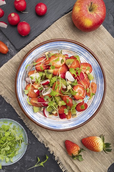 Vegetarian fruits and vegetables salad of strawberry, kiwi, tomatoes, microgreen sprouts on black