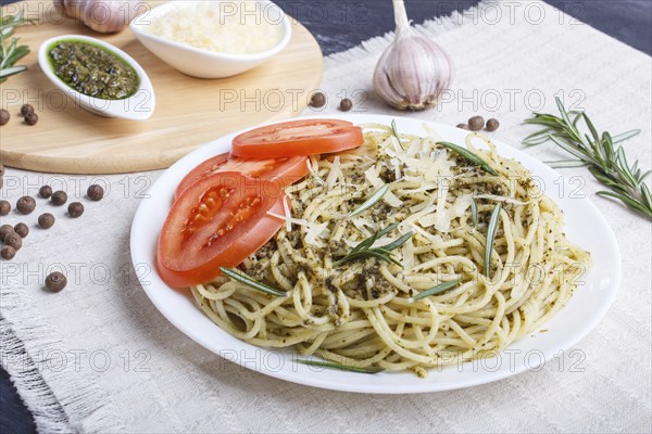 Spaghetti pasta with pesto sauce, tomatoes and cheese on a linen tablecloth on black wooden