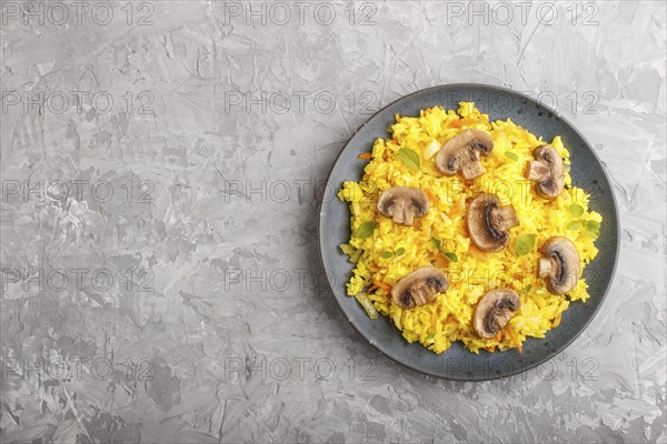 Yellow fried rice with champignons mushrooms, turmeric and oregano on blue ceramic plate on a gray