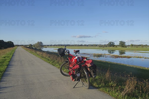 Red loaded bicycle on a road next to a wide landscape with water and sky, bicycle tourism,