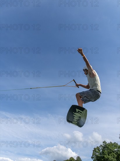 Young man jumping and flying with wakeboard, water sports and water skiing in the wakepark
