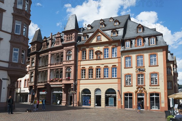 Multi-storey historic buildings with red facades and shutters surround a lively town square,