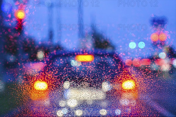 Blurred view of car lights at night through rain-soaked windows