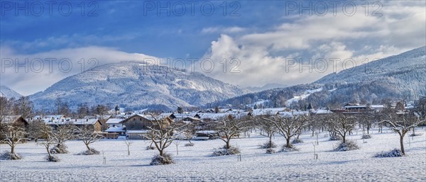 Snow-covered landscape with trees and village, in the background mountains under a blue sky, Bad