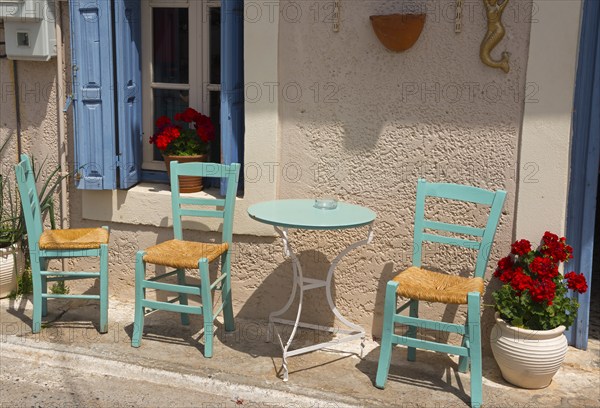 Cosy Mediterranean outdoor area with green chairs and blue shutters in front of a beige wall with